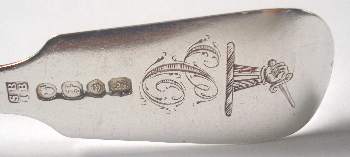 A silver spoon crest, with an arm, in armour, issuing, in hand a sword