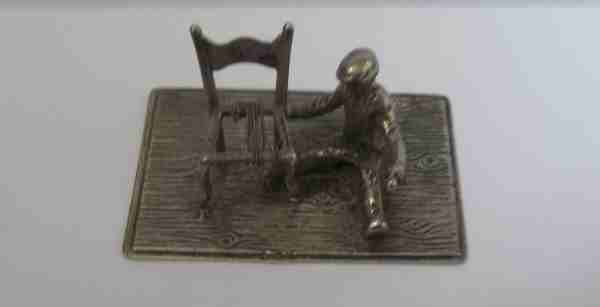 A Dutch silver miniature of a tradesman weaving the seat on a chair with flax covering